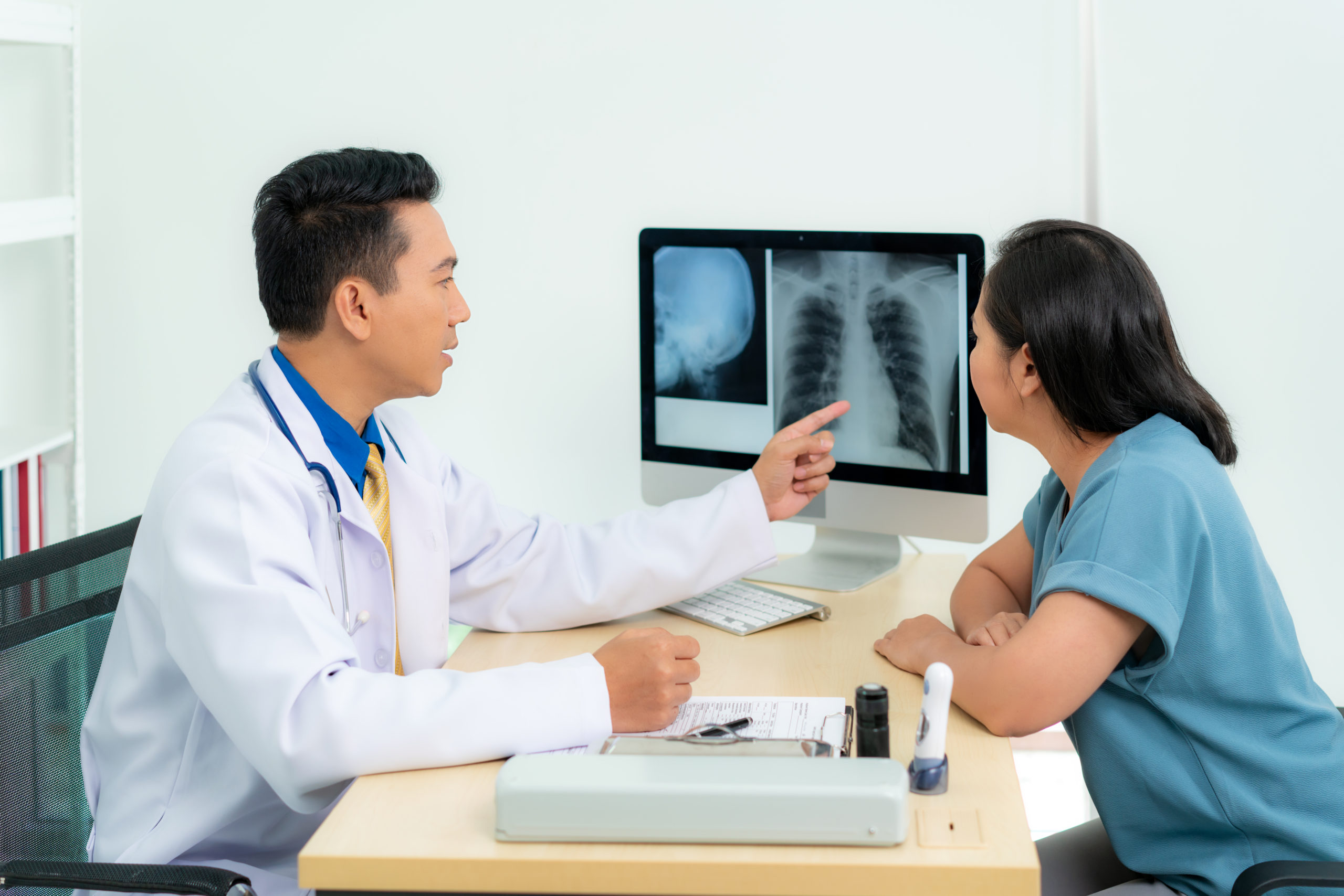 Asian doctor man medical diagnosis of lungs and reported bad news for cancer. Patient listening x-ray scan results from doctor at radiology at hospital.